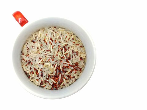 Top view of a cup of uncooked rice mix, comprising parboiled and basmati brown rice, and red quinoa, a product of bio agriculture, isolated on white background.