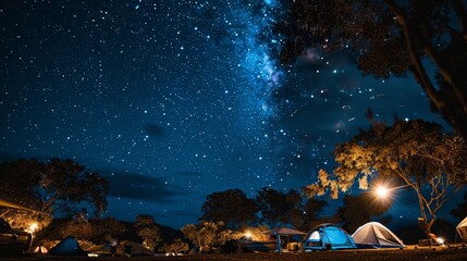 Obraz premium Starry night sky over a campsite with tents and trees illuminated by a warm light