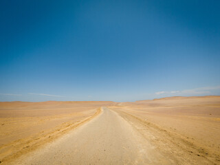 Desert road curving through sandy landscape under clear blue sky. Outdoor travel and adventure concept. Aerial view of desert route.