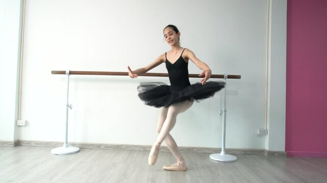 Young beautiful fourteen year old girl in black ballet tutu practicing ballet dancing practicing dancing as a black swan using bar pole, white wall in studio