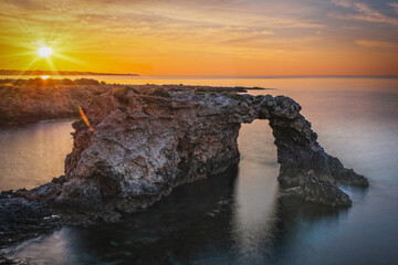 Rocky coastline with a natural arch at punta Asparano, near Siracusa. Sunrise time, long exposure...