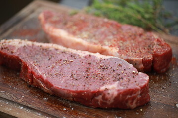 Seasoned raw steaks garnished with fresh thyme and rosemary on wooden board