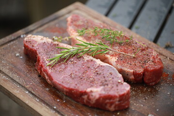 Seasoned raw steaks garnished with fresh thyme and rosemary on wooden board