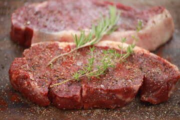 Seasoned raw steaks garnished with fresh thyme and rosemary on wooden board