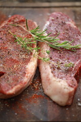 Seasoned raw steaks garnished with fresh thyme and rosemary on wooden board