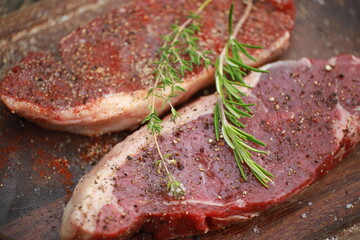 Seasoned raw steaks garnished with fresh thyme and rosemary on wooden board