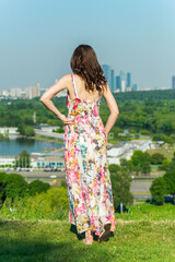 A young happy girl in a bright dress standing on a green grassy hillside on a sunny day enjoying...