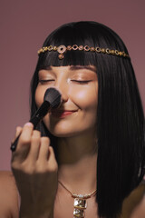 Glamorous Woman Applying Makeup with Cleopatra-Inspired Look
