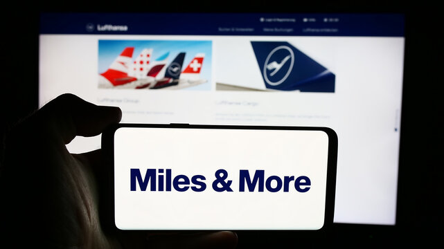 Stuttgart, Germany - 07-15-2024: Person holding cellphone with logo of frequent-flyer program Miles and More (Lufthansa) in front of business webpage. Focus on phone display.