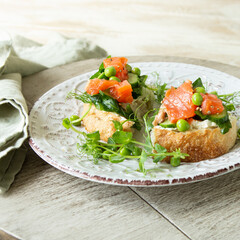 plate with bruschetta with soft cheese, salmon, cucumber and green peas on a light table