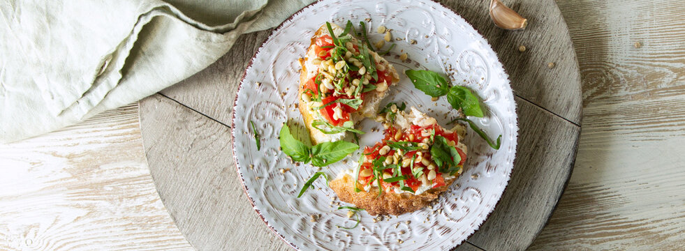 plate with bruschetta with soft cheese, concasse tomatoes and basil on a light table