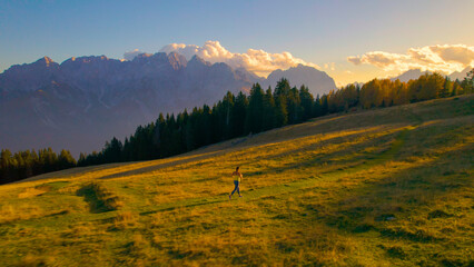 AERIAL: Athletic young lady is jogging along picturesque alpine meadow at sunset