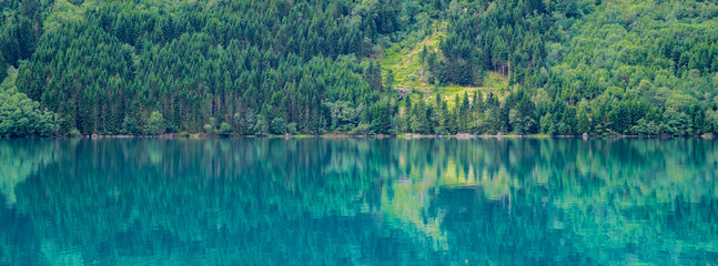 A serene lake in Norway, with a lush forest reflected in the crystal clear water. lovatnet lake Lodal valley Norway