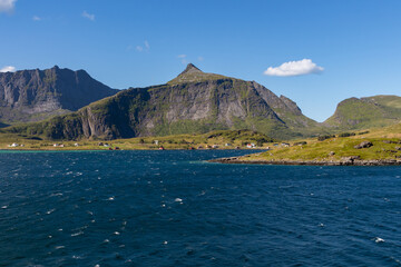 Coast with houses on the shore with high green mountain in the background
