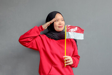 Beautiful Asian muslim woman saluting celebrating Indonesia's independence day on August 17 isolated on gray background