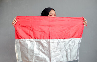 Beautiful Asian muslim woman saluting celebrating Indonesia's independence day on August 17 isolated on gray background