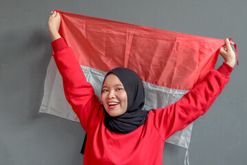 Beautiful Asian muslim woman saluting celebrating Indonesia's independence day on August 17 isolated on gray background