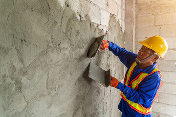 Asian worker using a trowel to apply cement plaster to a wall, meticulously working on the exterior...
