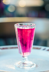A glass of pink liquid is on a white plate