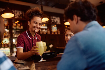 Happy waitress serving drinks to group of guests in  bar.