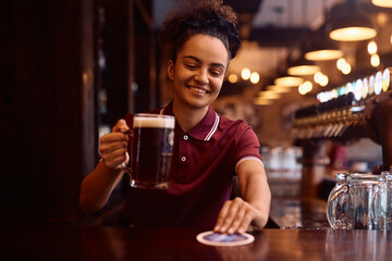 Happy waitress serving beer at bar counter in  pub.