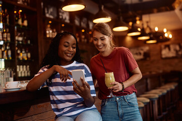 Happy female friends using smart phone in pub.