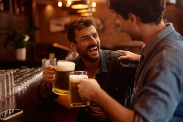Cheerful male friends toasting with beer in bar.