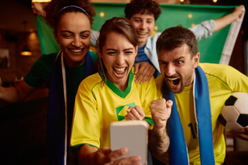 Excited soccer fans cheering while watching match on smart phone.