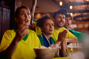 Group of friends watching sports match on TV while drinking beer in pub.