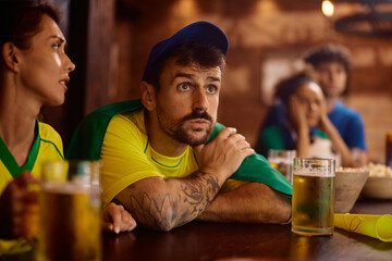 Sports fan watching  match with anticipation while drinking beer in pub.