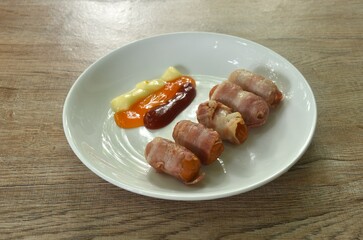 pork sausage roll up bacon dipping mayonnaise and chili sauce with ketchup arranging on plate