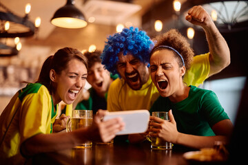Excited sports fans watching  match on mobile phone and shouting after the winning goal of their favorite team.