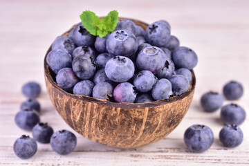 Fresh blueberry berries in a coconut shell bowl on a white wooden background.
