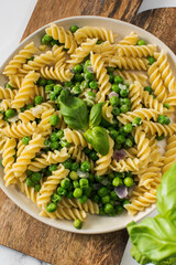 Tasty pasta with green peas and basil on white marble table