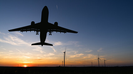 Silhouette of landing plane with wind turbines. Clean mobility concept.