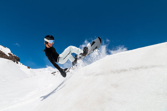 Young pro snowboarder riding the half pipe in mountain snow park, sliding and spraying on the halfpipe wall in sunny winter