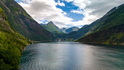 A stunning view of a fjord in Norway, surrounded by verdant mountains and a clear blue sky....