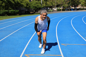 Senior Asian athlete is practicing running with relay baton in the professional blue track for...