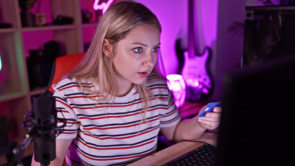 Focused young woman holding credit card while using computer in neon-lit room at night.