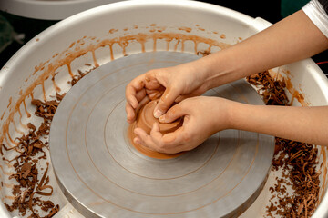 Children's hands create pottery on a potter's wheel during a master class on an outdoor playground