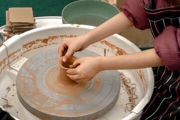 Fototapeta premium Children's hands create pottery on a potter's wheel during a master class on an outdoor playground