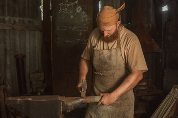 Mechanic in a bandana straightens a metal pipe with a hammer on an anvil in a street workshop. Close-up