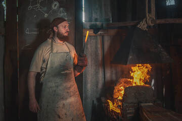 Blacksmith heats a metal part in a fire before forging it in an old village forge. Traditional...