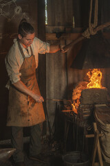 Blacksmith heats a metal part in a fire before forging it in an old village forge. Traditional...