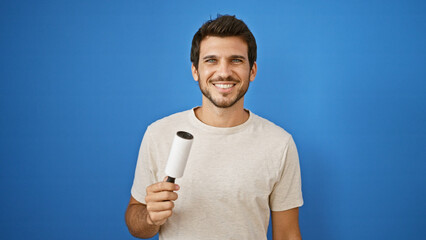 Smiling young hispanic man holding a microphone against a blue isolated background