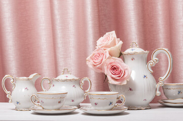 Coffee set on white wooden table with live flower heads of pink roses on pink background.