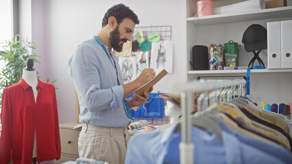 Obraz premium A bearded man takes notes in a tailor shop among racks of fabrics and clothes, reflecting craftsmanship and design.