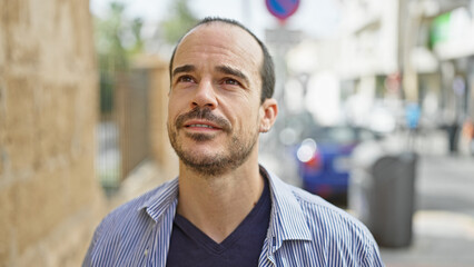 Hispanic bald man with beard in urban city street setting, exemplifying outdoor lifestyle.