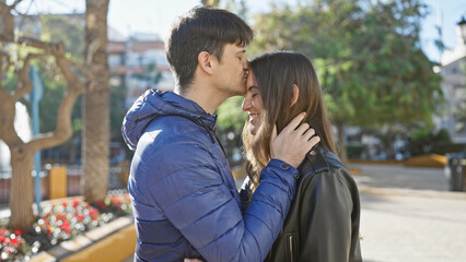 Fototapeta premium A couple embraces lovingly on a sunny city street surrounded by nature and urban elements.