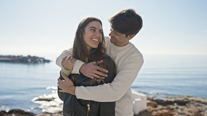 A loving couple embraces by a tranquil sea, exuding romance and happiness in a picturesque outdoor setting.